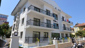 A multi-story building with balconies, a sign indicating availability for rent, and a clear blue sky. - Artim Exclusive Apart Hotel (Fethiye)