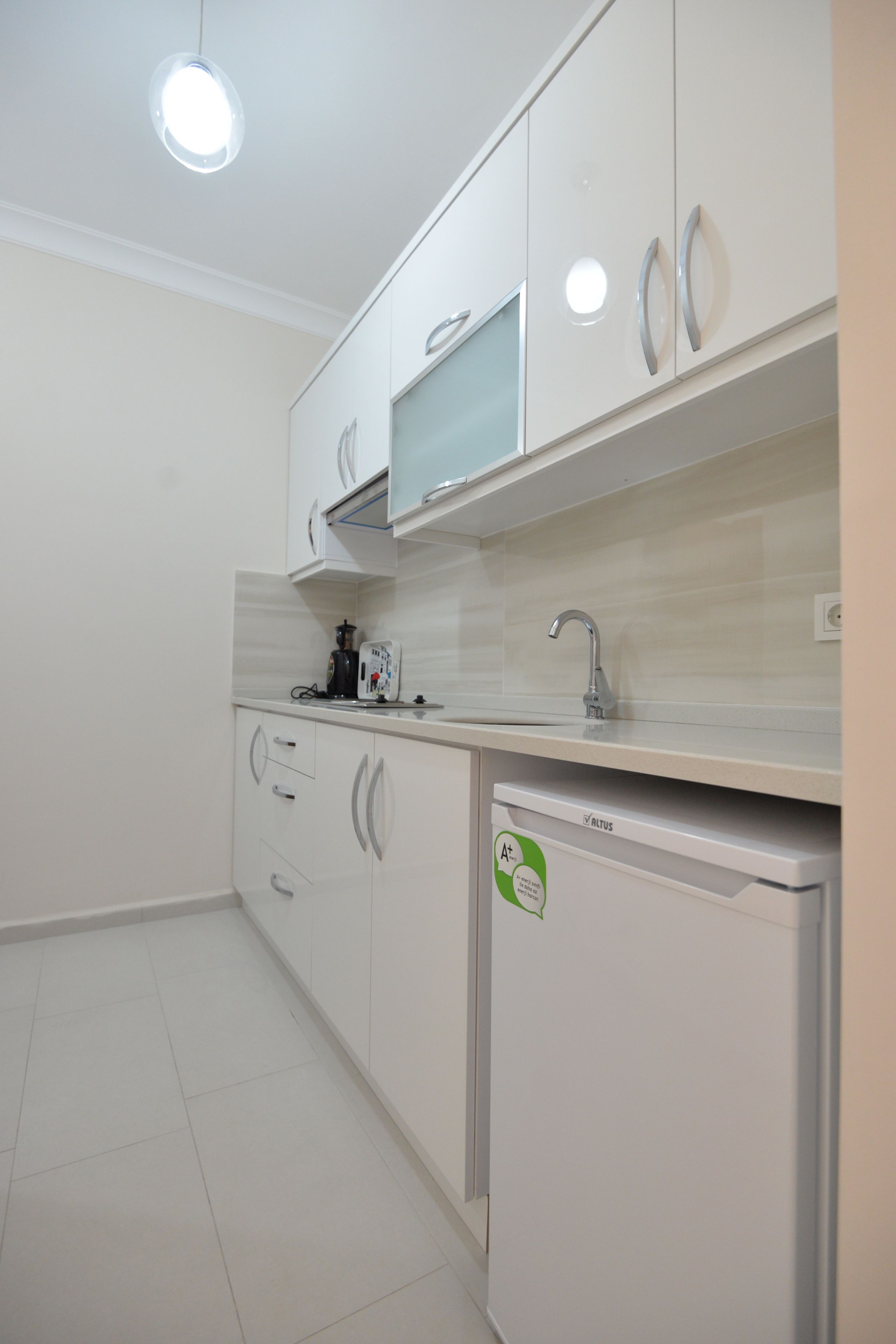 A modern kitchen with white cabinets, a built-in oven, and a small refrigerator.