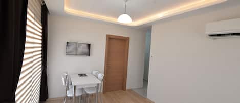 Uma sala de jantar moderna com uma mesa e cadeiras brancas, uma luminária no teto e um aparelho de ar condicionado.
