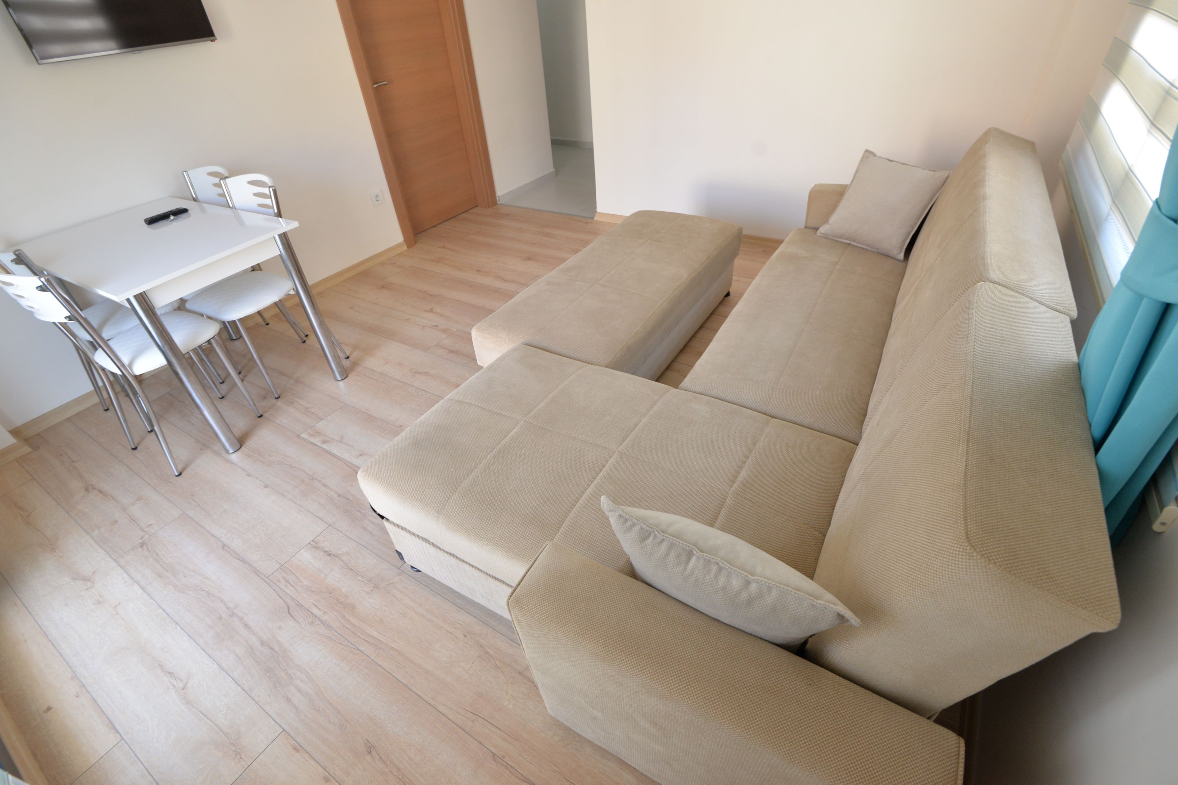 A modern living room with a beige sofa, a small white table with chairs, and a wooden floor.