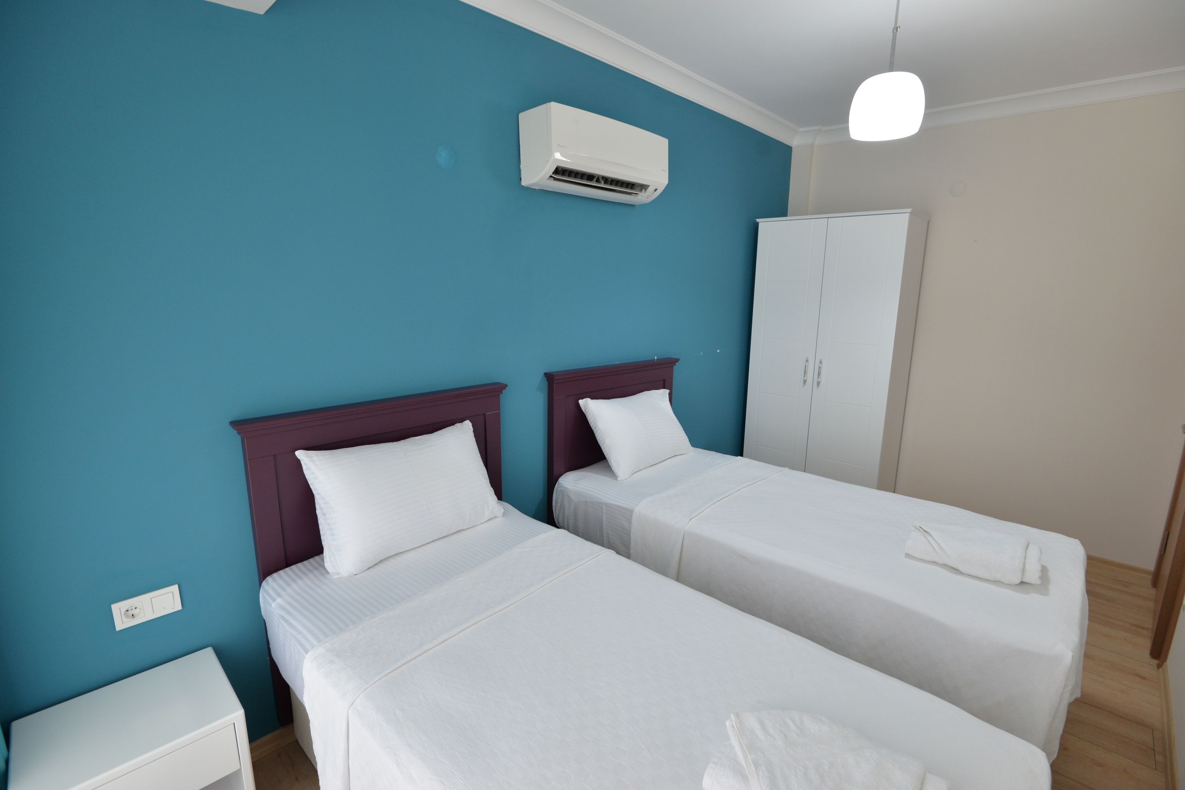 Hotellihuone, jossa on kaksi erillistä sänkyä, vaatekaappi, ilmastointilaite ja yöpöytä.