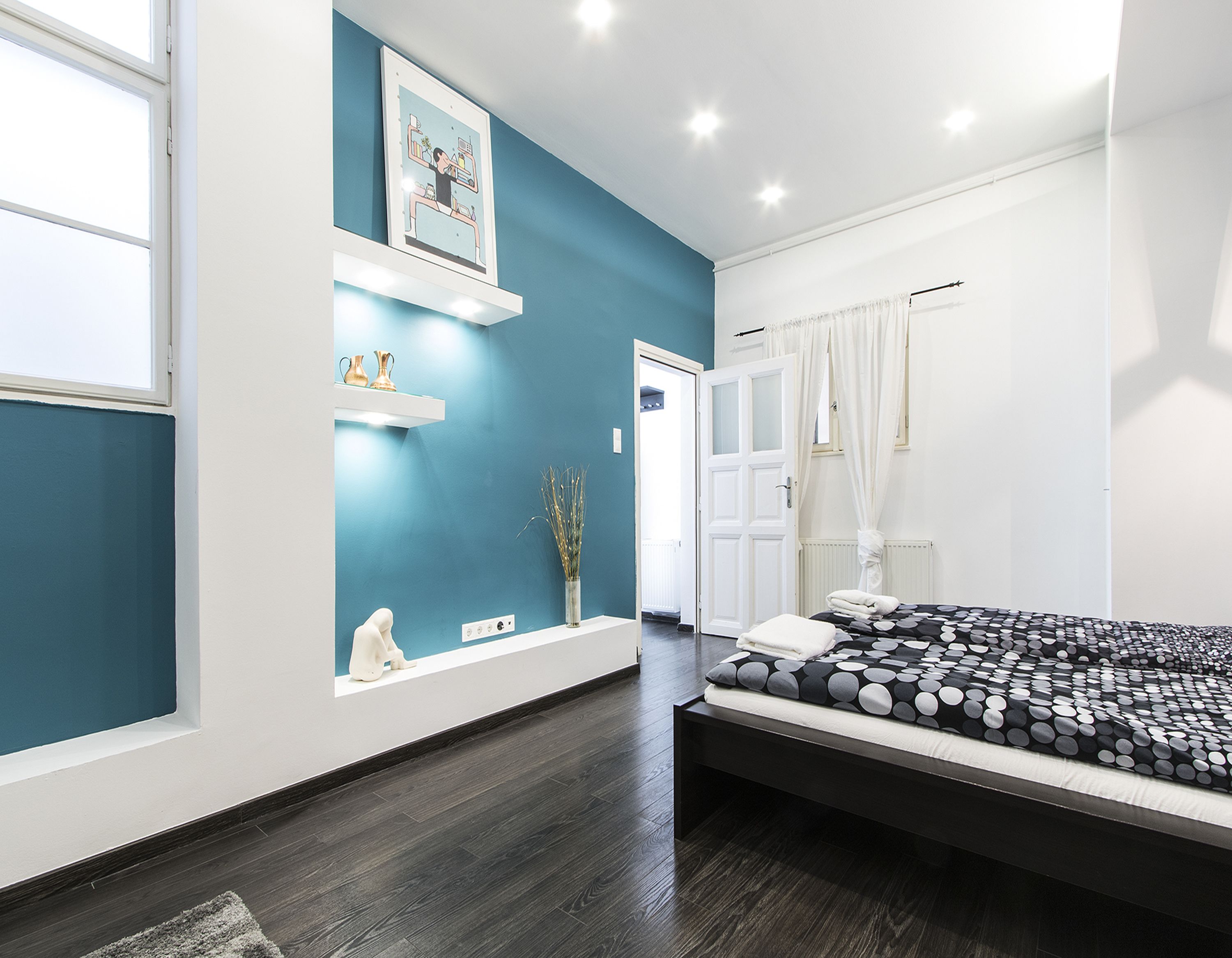 Une chambre à coucher avec un lit, une étagère ornée d’objets décoratifs, une porte et une fenêtre.