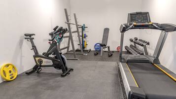 A gym with a stationary bike, treadmill, weight rack, and dumbbells.