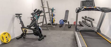 A gym with a stationary bike, treadmill, weight rack, and dumbbells.