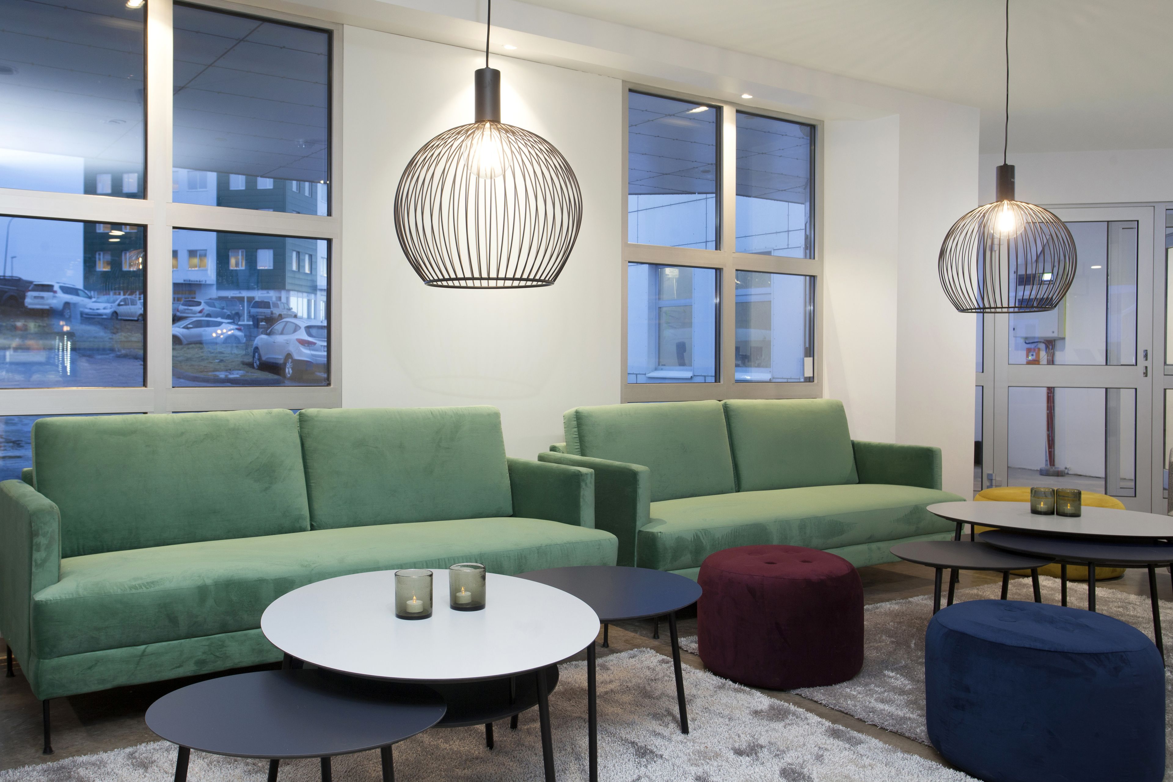 A modern living room with green sofas, round coffee tables, and pendant lighting.