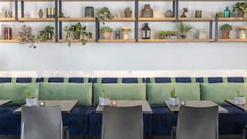 A seating area with a green sofa, wooden shelves with plants and decorative items, and a table with chairs.
