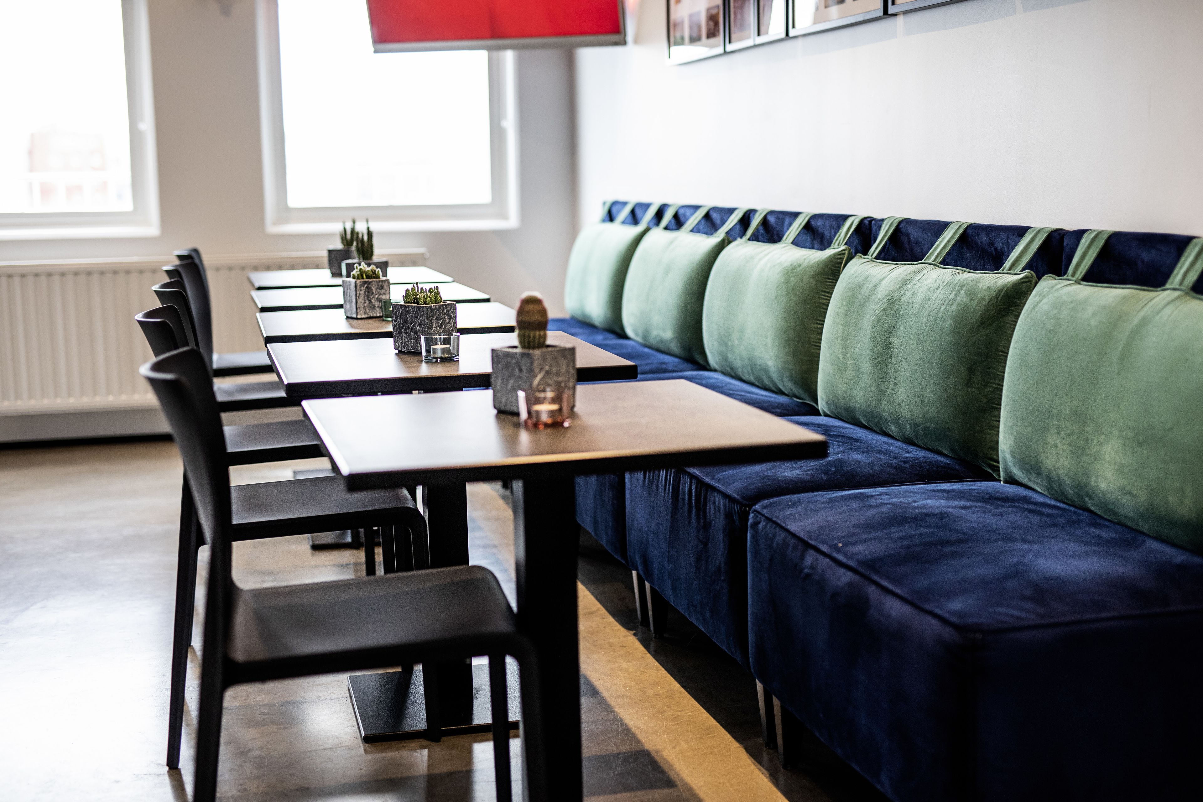 Un comedor moderno con una mesa larga, sillas negras y un sofá azul con cojines verdes.