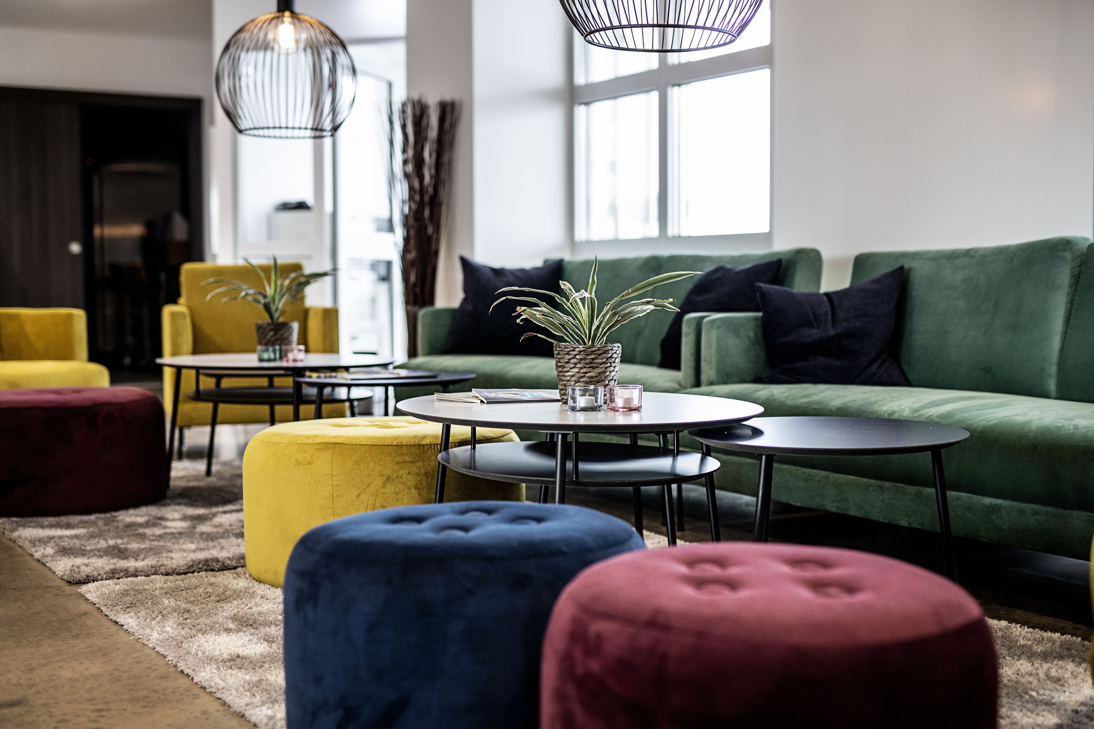 A modern living room with a green sofa, round coffee tables, and colorful ottomans.