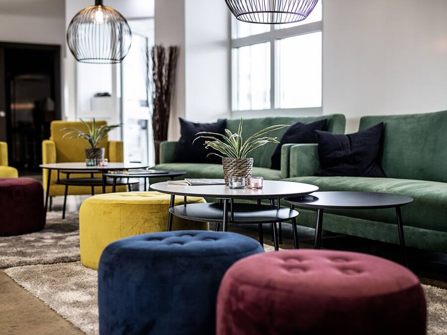A modern living room with a green sofa, round coffee tables, and colorful ottomans.