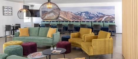 Un espace de détente moderne avec des canapés verts et jaunes, des poufs ronds et une grande fresque représentant des montagnes en arrière-plan.