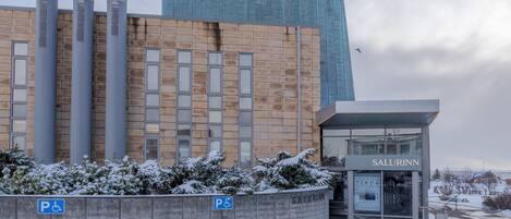 A building with a modern facade, a parking area with a disabled parking sign, and a sign for 'SALURINN'.