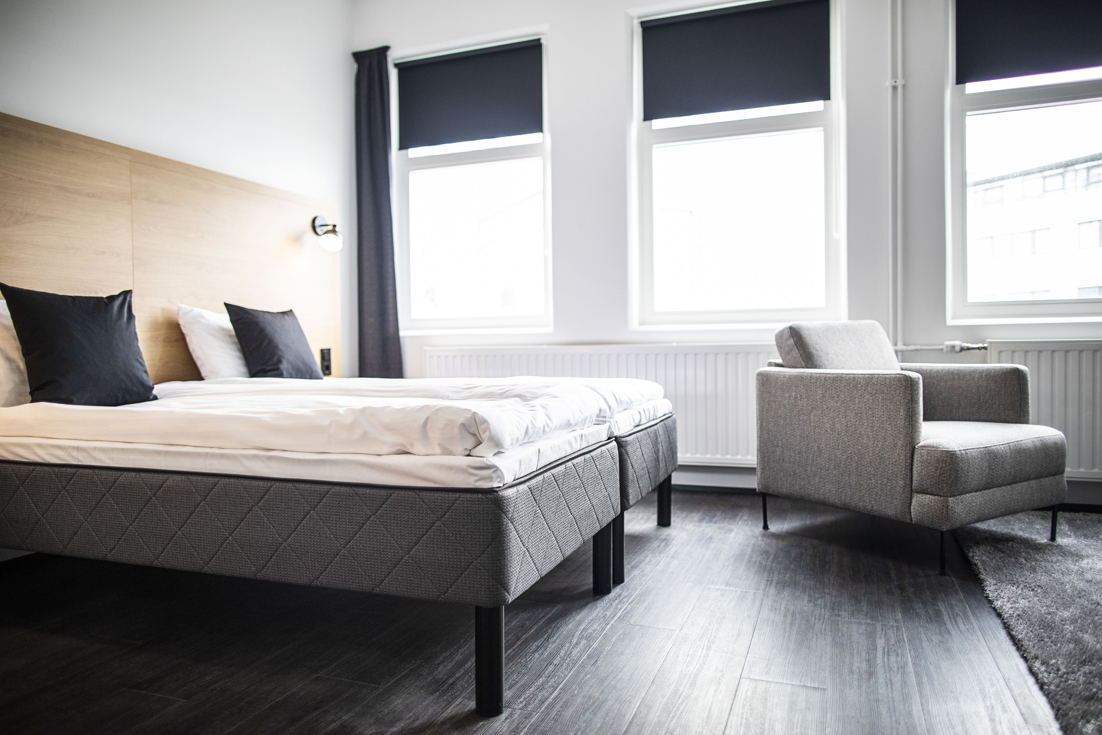 A modern bedroom with a bed, a chair, and large windows.