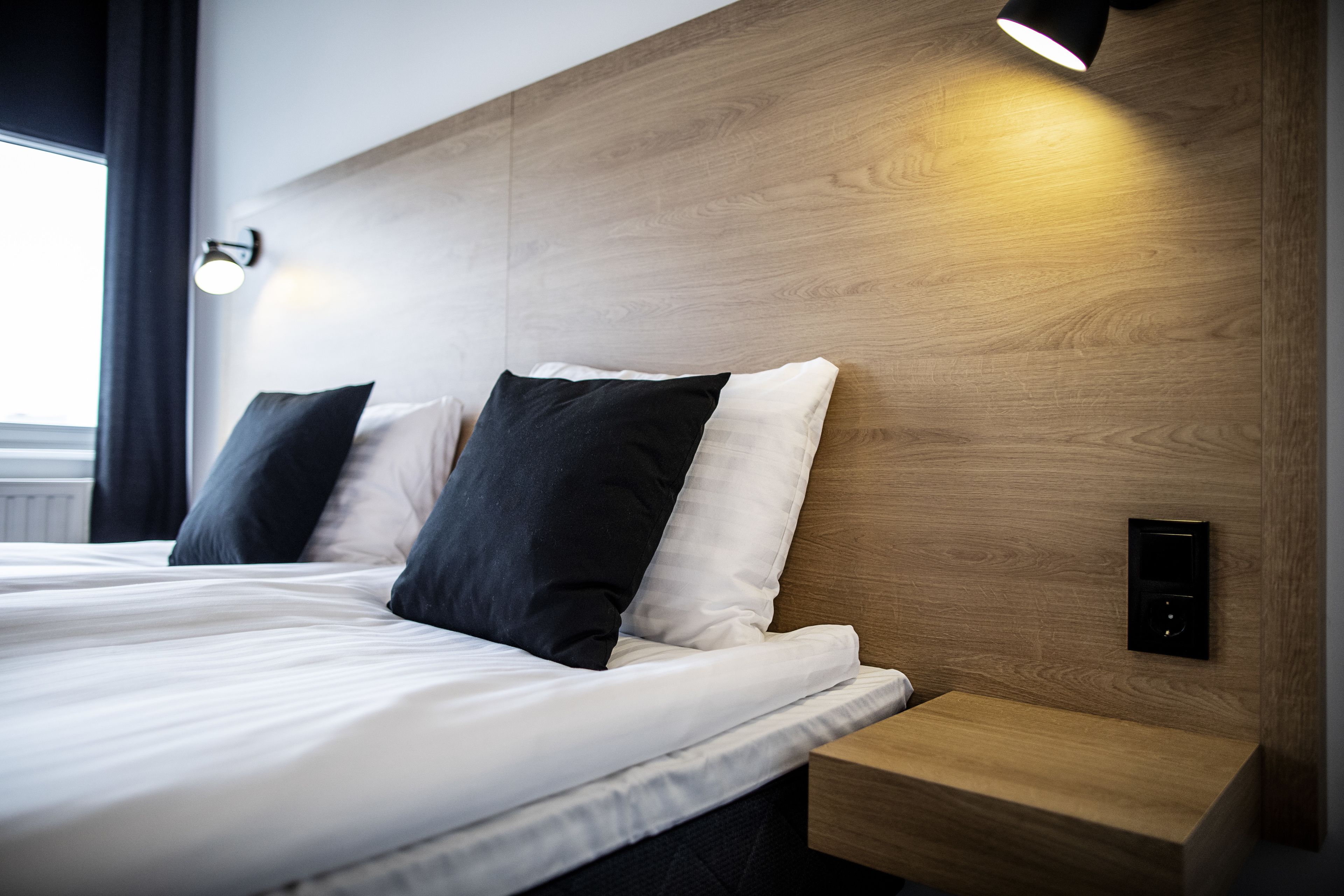 Une chambre d’hôtel moderne avec une tête de lit en bois, une table de chevet et un panneau de commande.