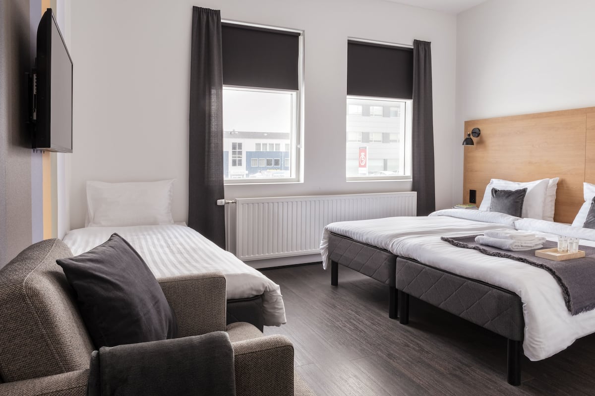 A hotel room with two beds, a sofa, and a TV.