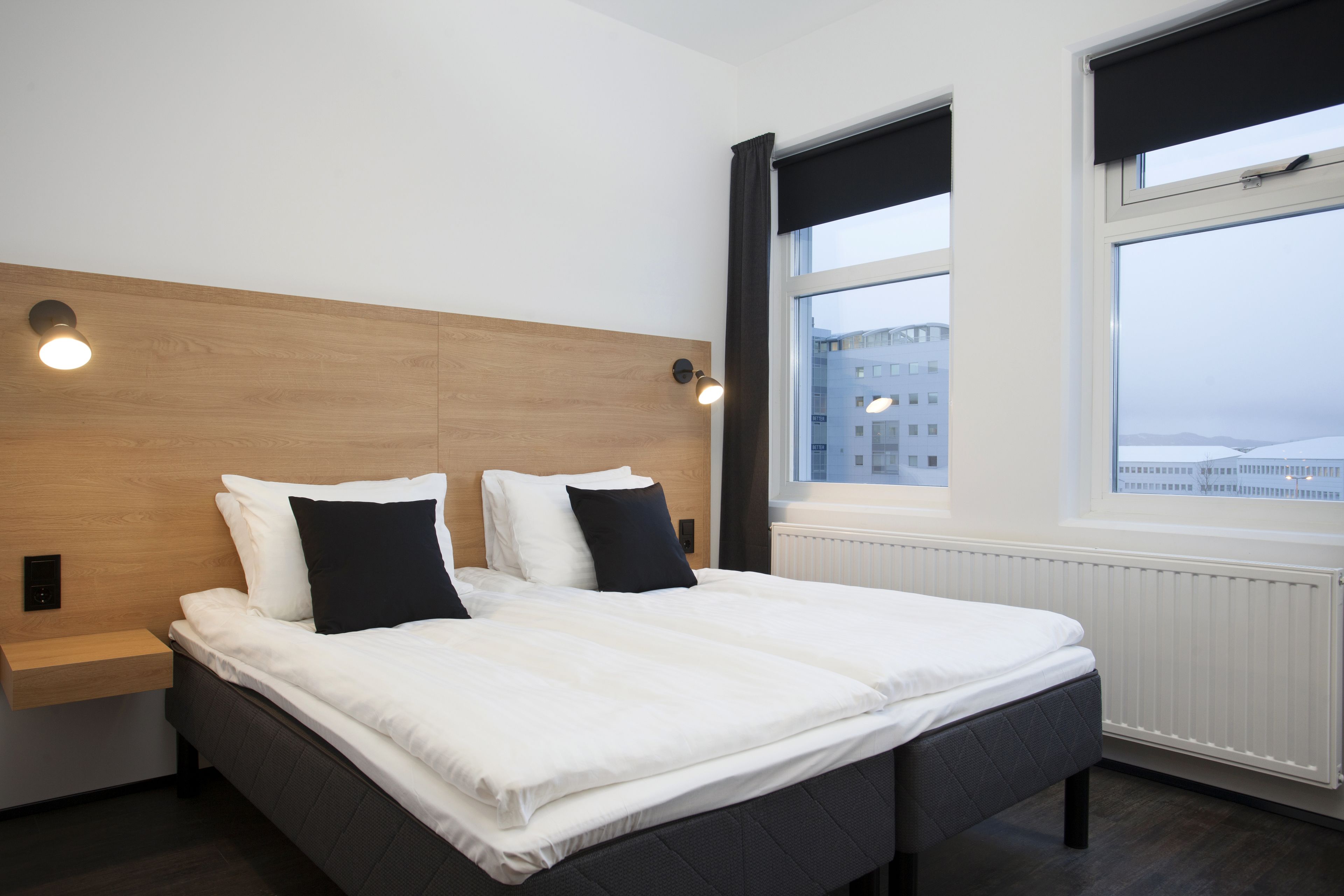 A modern hotel room with a large bed, bedside tables, and a window with a view of buildings.