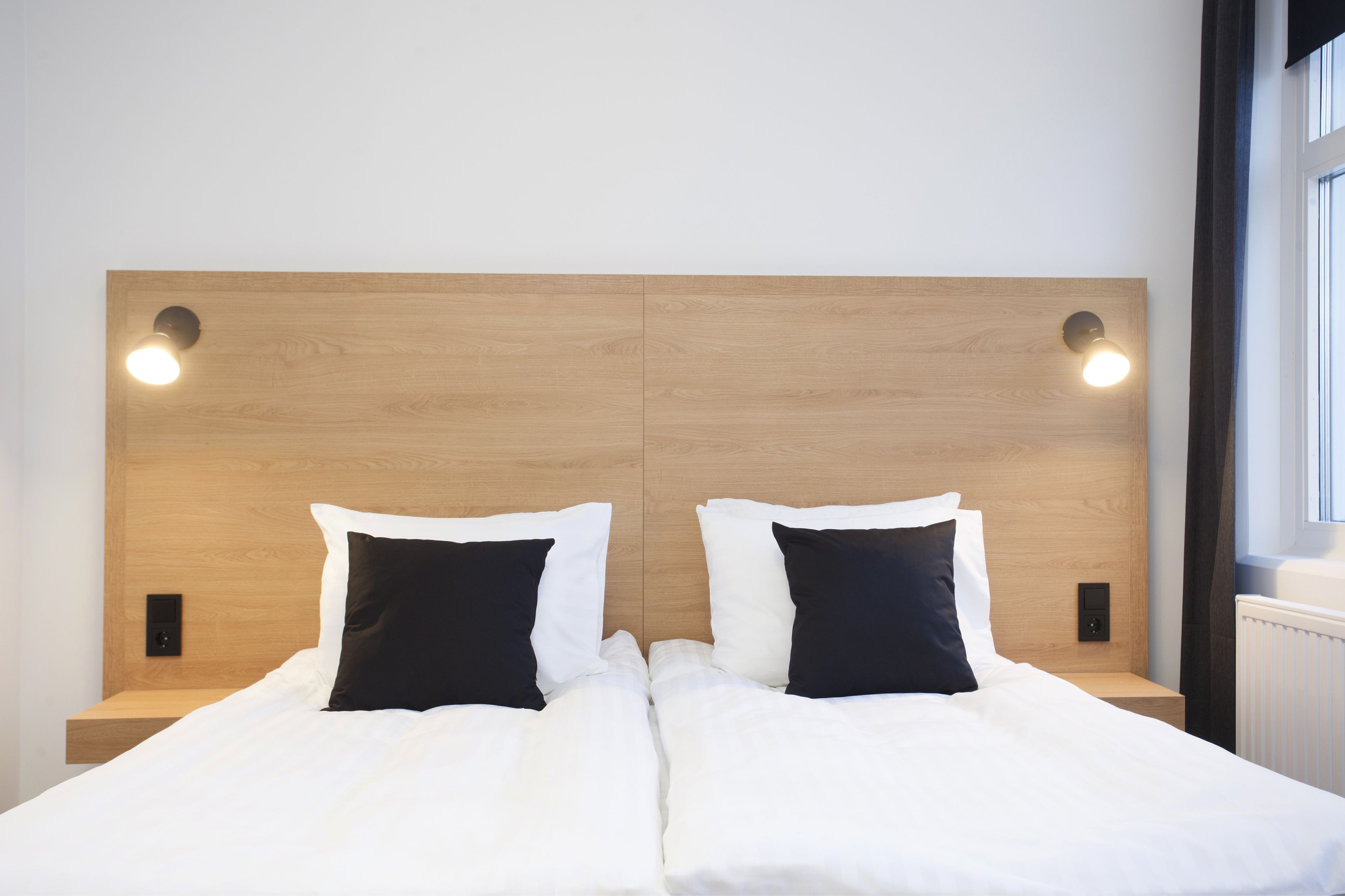 A double bed with white and black bedding, a wooden headboard, and two bedside lamps.