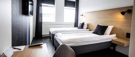 A hotel room with two beds, a desk, a chair, a TV, and a window with curtains.