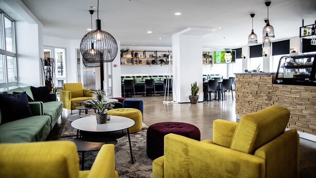 A modern interior with a green sofa, yellow armchairs, and a round coffee table. - 201 Hotel (Kópavogur)