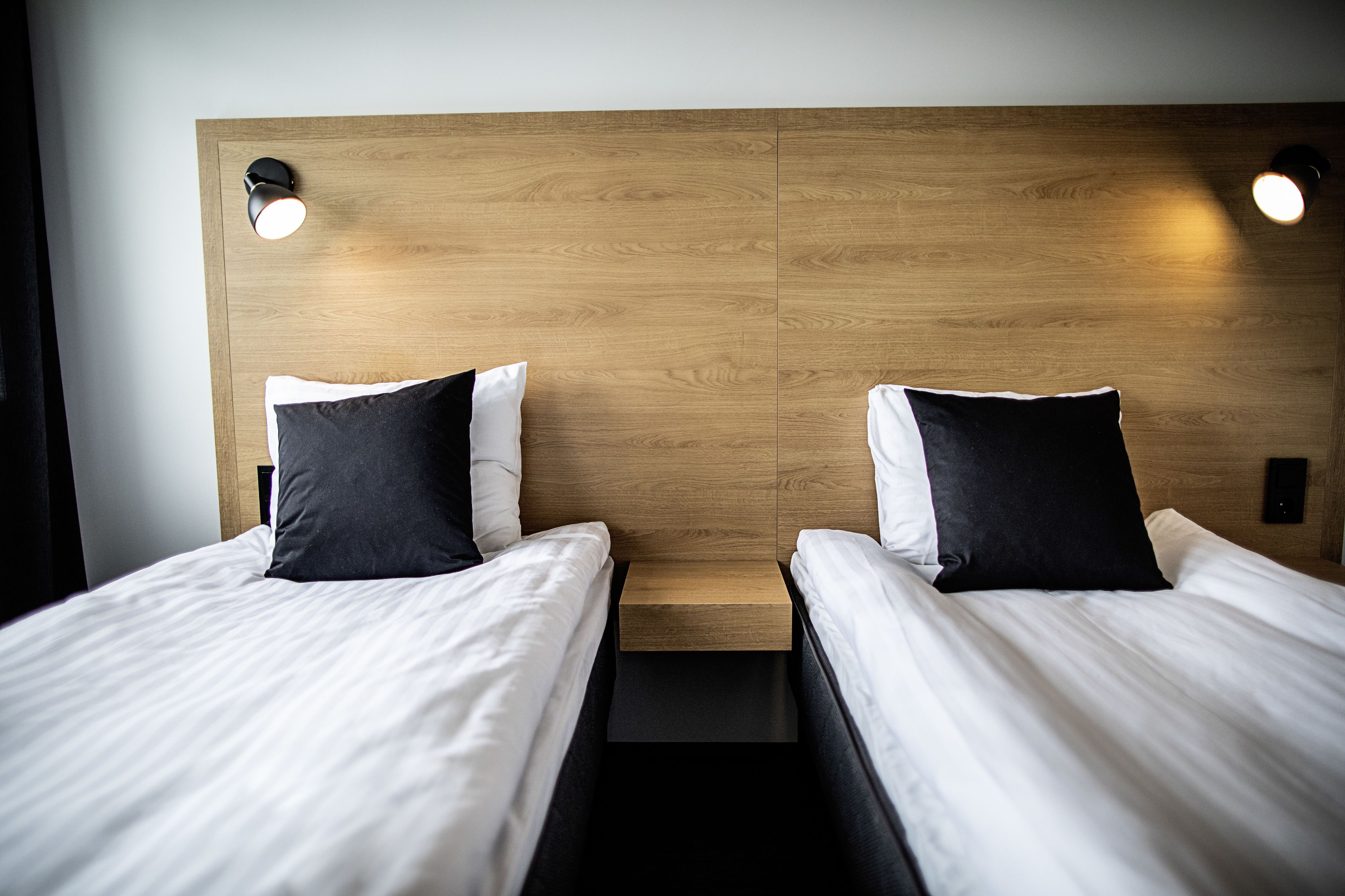 Two single beds with white bedding and black pillows, a wooden headboard, and two wall-mounted lights.