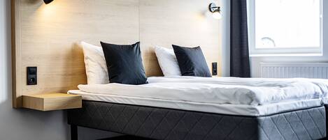 Un dormitorio moderno con cabecera de madera, una cama con colchón gris acolchado, dos almohadas negras y lámparas de noche.