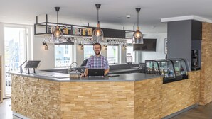 A modern bar area with a wooden counter, hanging light fixtures, and a large window providing a view of the cityscape. - 201 Hotel (Kópavogur)