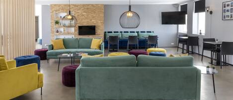 Una sala moderna con sofás verde y amarillo, una pared de ladrillo decorativa y un televisor de pantalla plana.