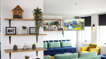 Ein modernes Wohnzimmer mit einem Ecksofa, bunten Hocker und Regalen mit Pflanzen und Dekoration.