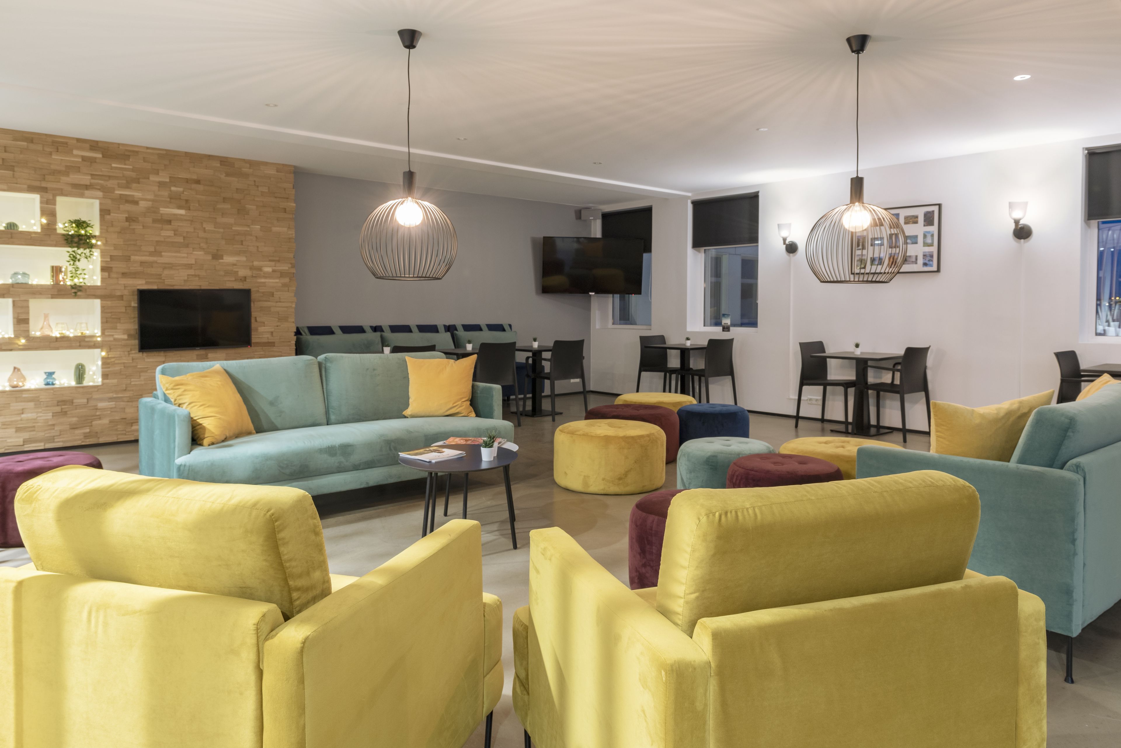 A modern living room with a sofa, armchairs, ottomans, and a flat-screen TV mounted on the wall.