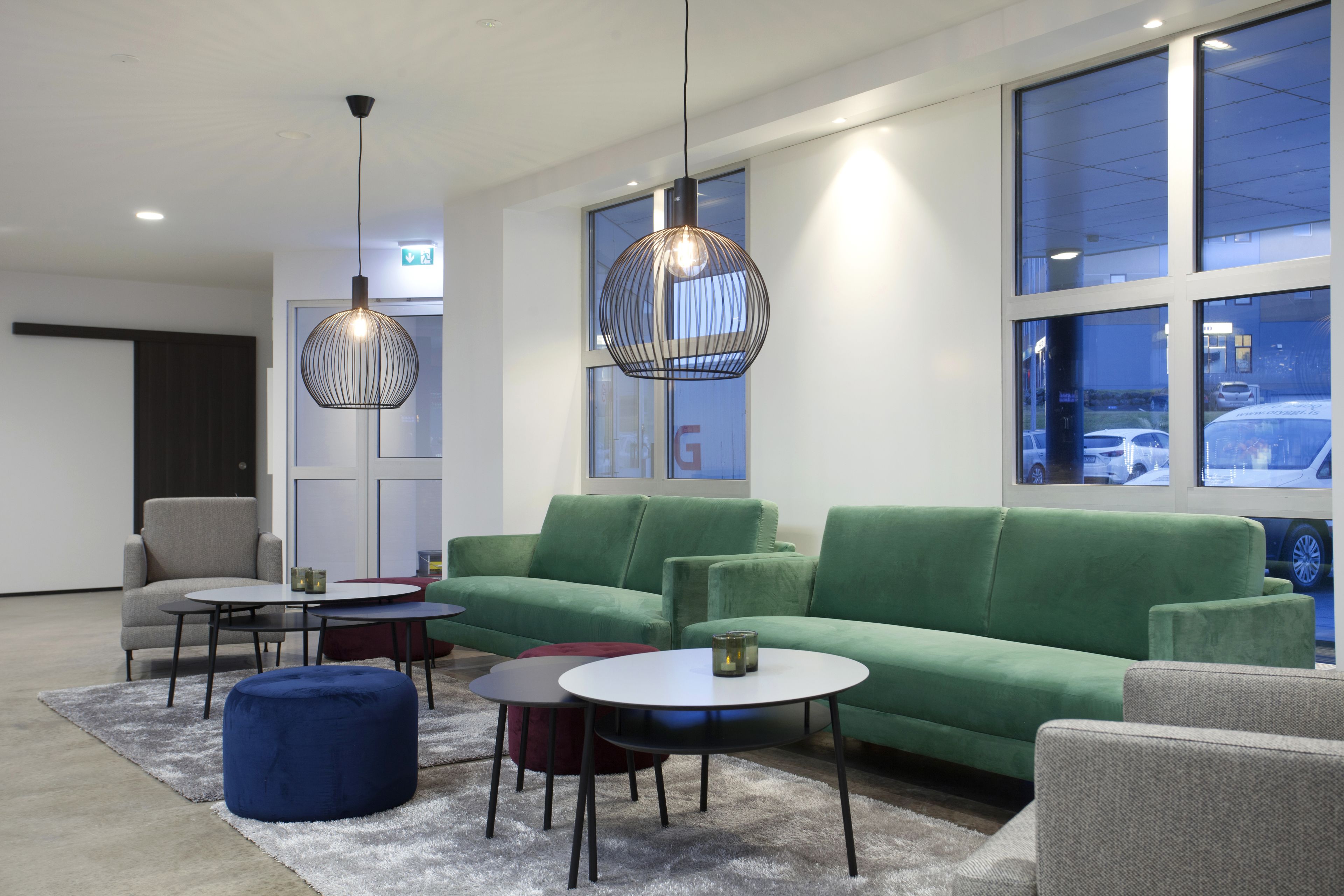 Un espacio lounge moderno con sofás verdes, mesas redondas e iluminación colgante.