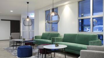 Un espace de détente moderne avec des canapés verts, des tables rondes et des luminaires suspendus.