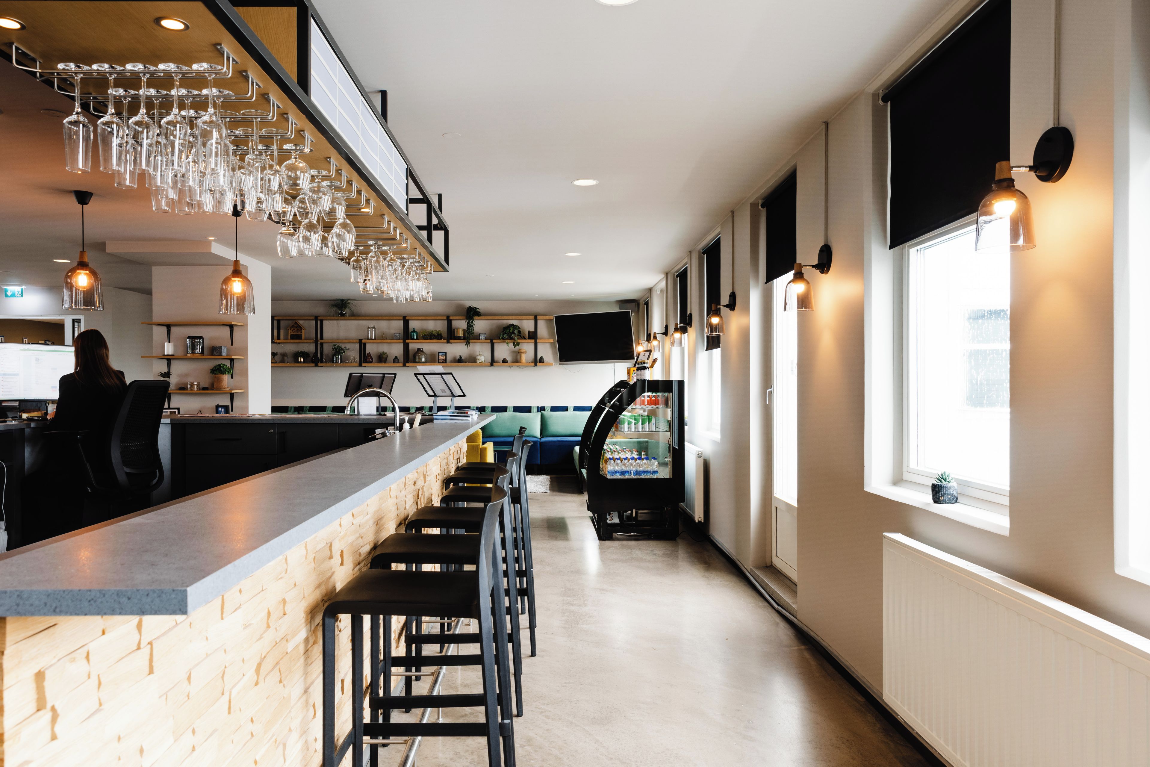 A bar area with a long counter, multiple stools, and a hanging light fixture with wine glasses.