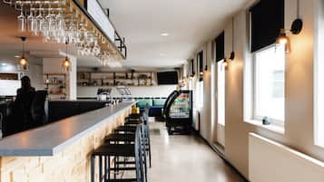 A bar area with a long counter, multiple stools, and a hanging light fixture with wine glasses.