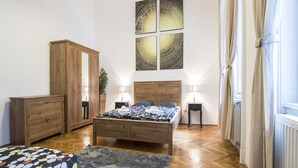 Un dormitorio con cama de madera, mesitas de noche, un armario y un amplio ventanal con cortinas.