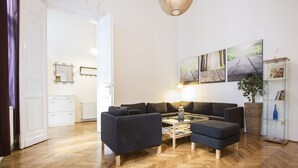 Una sala de estar moderna con piso de madera en espiga, un sofá modular de color oscuro, una mesa de centro de vidrio y una lámpara colgante.