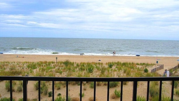 A beach with a view of the ocean, a sandy area with some vegetation, and a railing in the foreground. - Worcester House 302 (Ocean City)