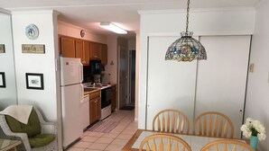 A compact kitchen with wooden cabinets, a refrigerator, and a dining area with a table and chairs. - Worcester House 302 (Ocean City)