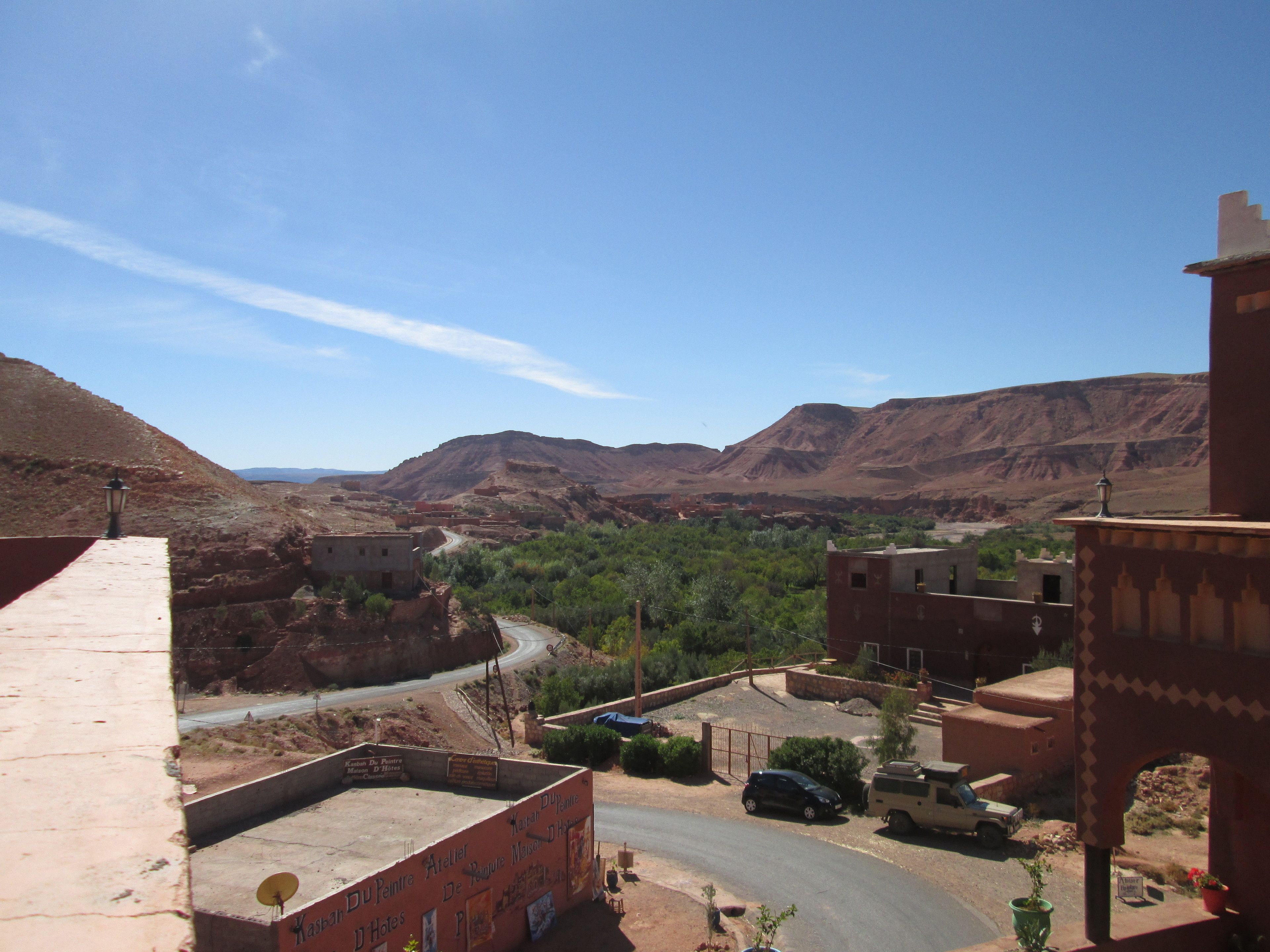 A desert landscape with buildings, a road, and mountains in the background.