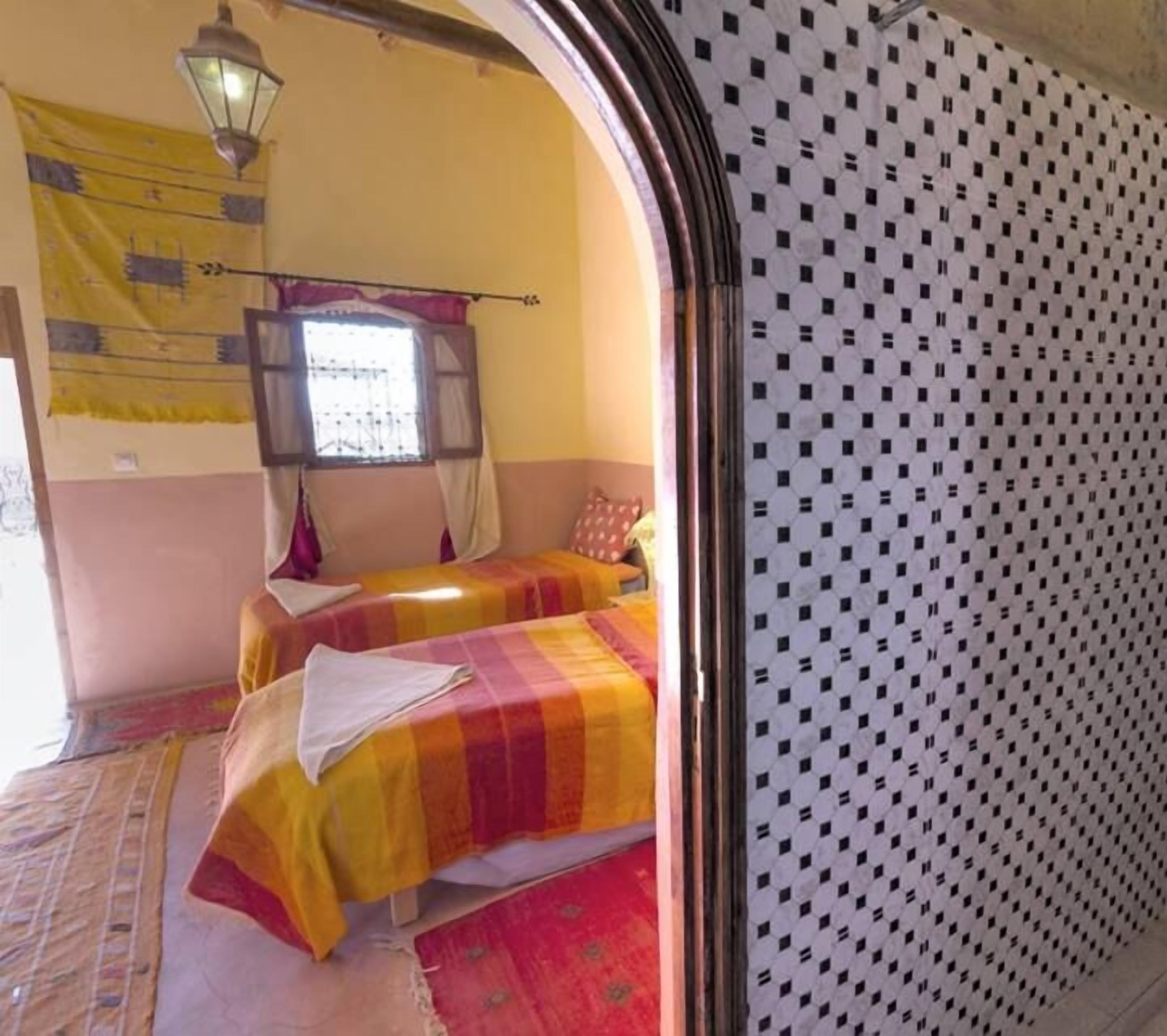 Ein Zimmer mit zwei Betten, einem Vorhangfenster, einer gemusterten Wand und einer Hängeleuchte.
