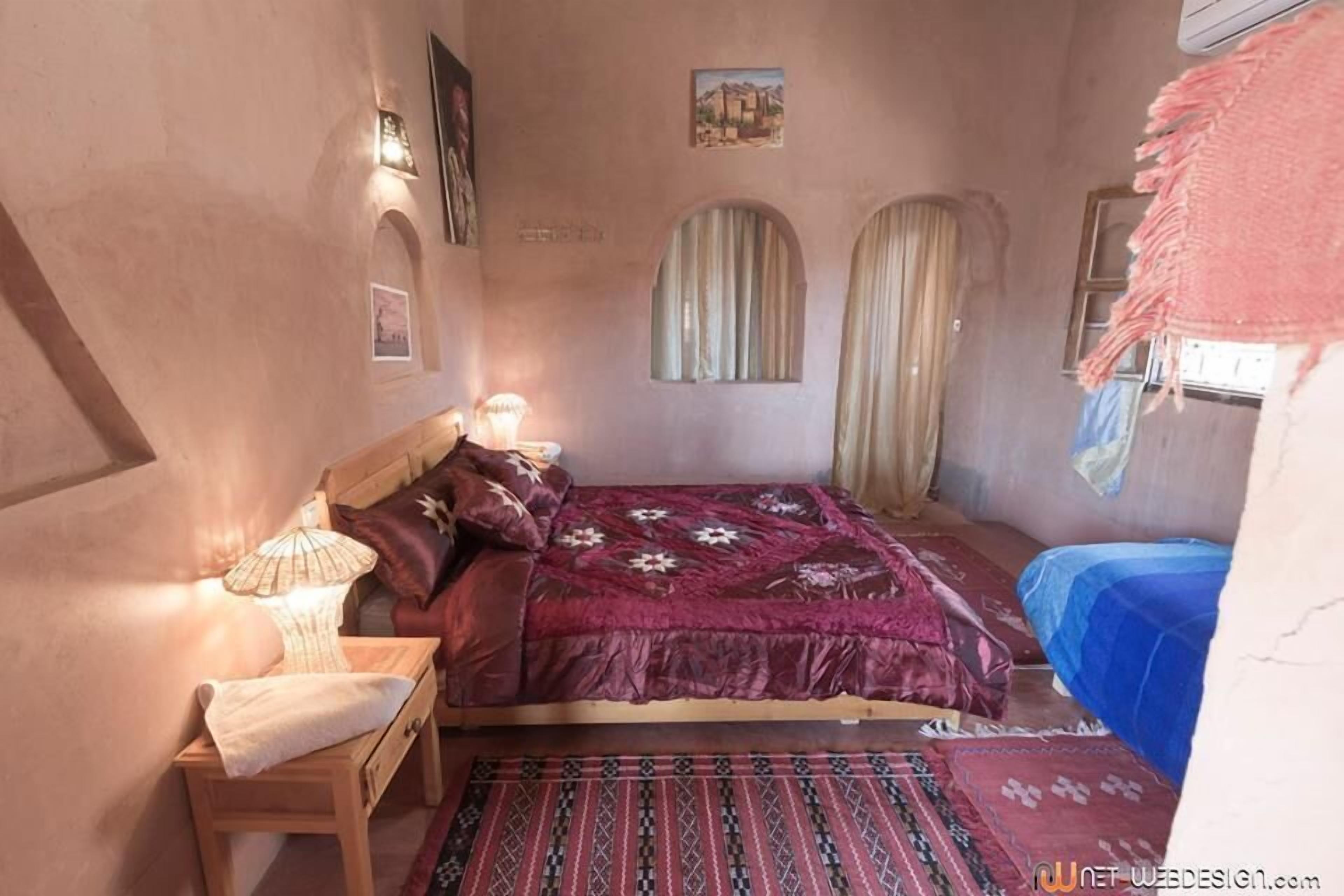 A bedroom with a bed, a nightstand, a lamp, and a window with curtains.