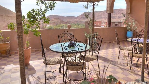 Un patio al aire libre con piso a cuadros, sillas de metal y una mesa con un centro de mesa decorativo.