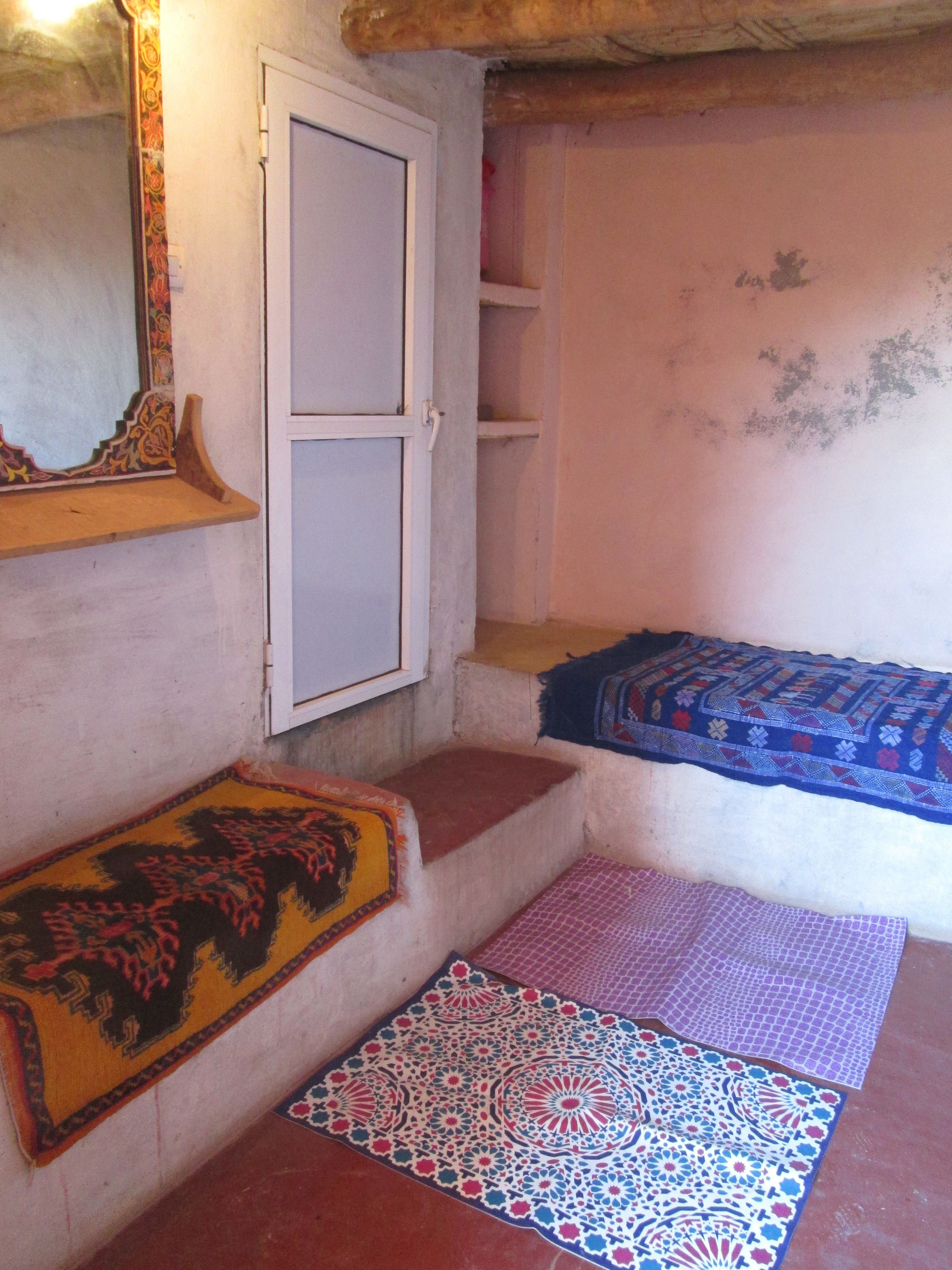 A room with a bed, a wardrobe, a mirror, and a patterned rug.