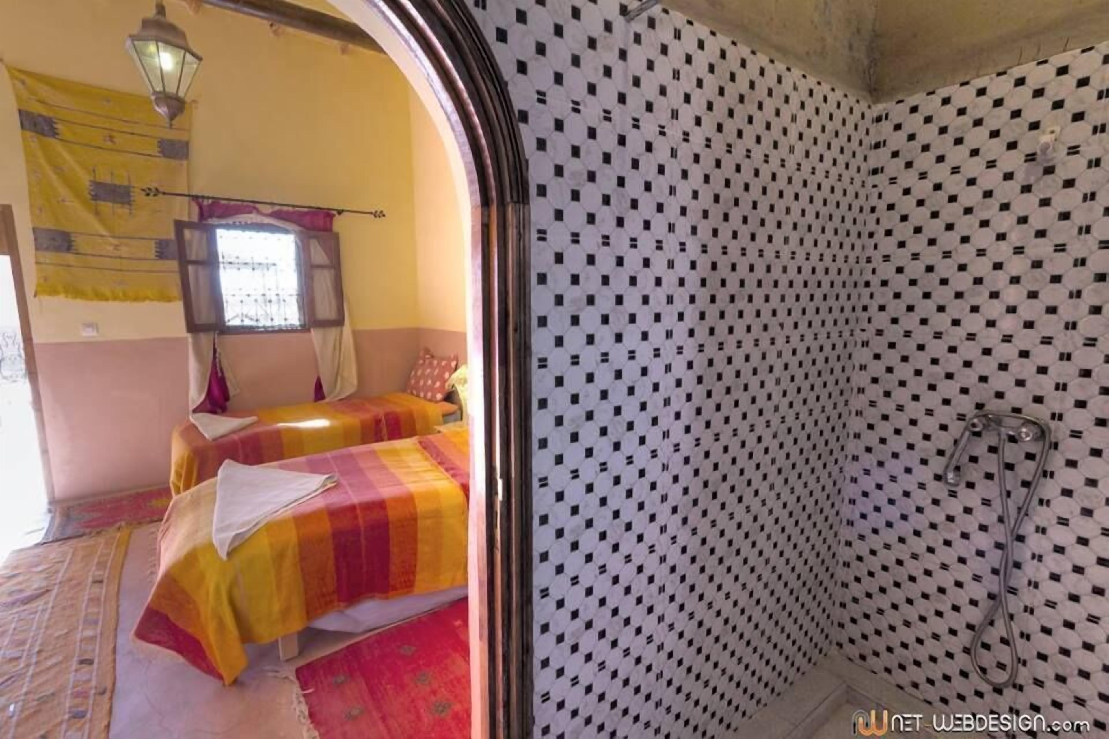 A room with two beds, a patterned shower wall, and a hanging light fixture.