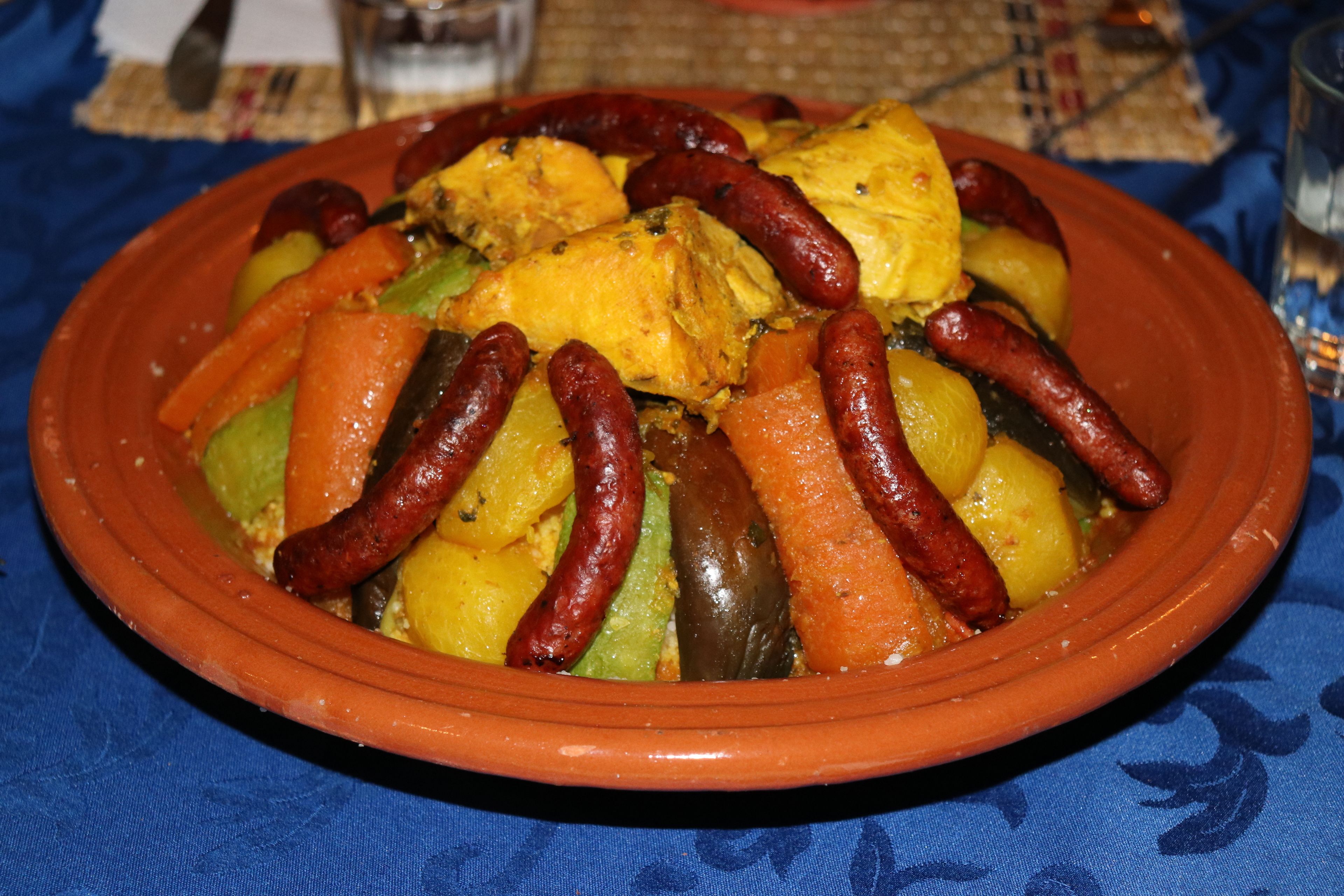A traditional clay pot filled with a variety of vegetables and sausages, likely a Moroccan tagine dish.