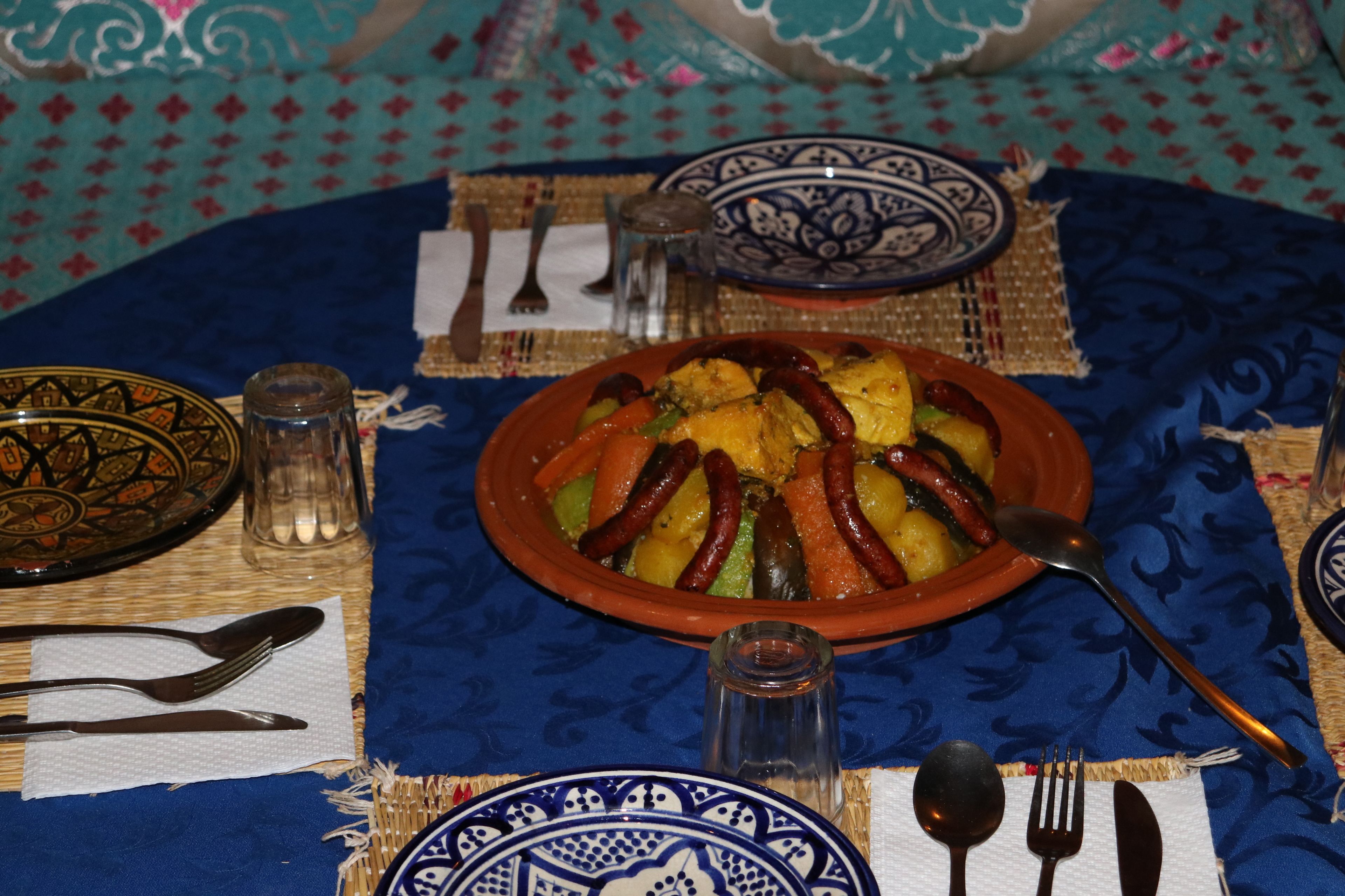Una mesa dispuesta con comida tradicional, incluyendo una olla de barro con verduras y carnes, y diversos utensilios.