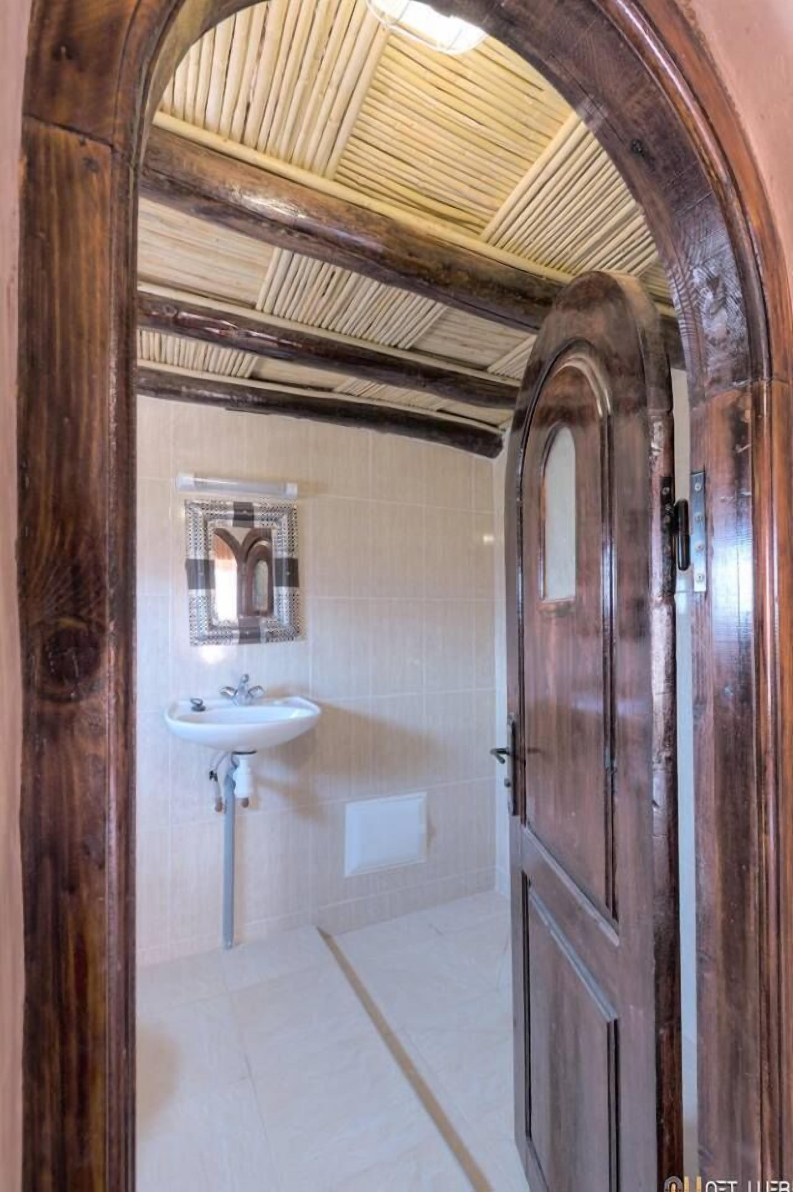 A wooden door leading to a bathroom with a white sink and a towel rack.