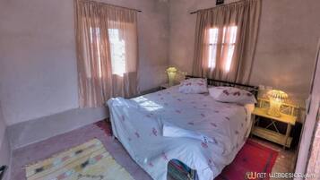Un dormitorio con cama, cortinas, una mesita de noche y una lámpara.
