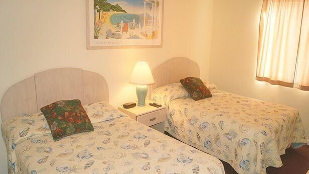 A room with two single beds, each with a floral-patterned bedspread, a nightstand with a lamp, and a painting of a beach scene on the wall. - Eagle Bay 204 (Ocean City)