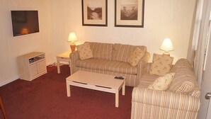 A living room with a striped sofa, two lamps, a television, and a small cabinet. - Eagle Bay 204 (Ocean City)