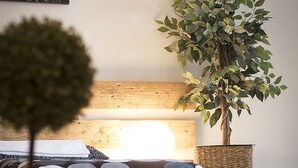 Un dormitorio ordenado con una cama, una pequeña planta en maceta y una obra de arte en la pared.
