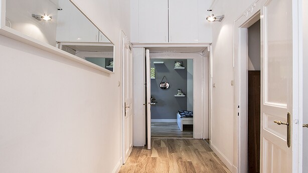 Un pasillo con suelo de madera, paredes blancas y puertas que dan a un dormitorio.